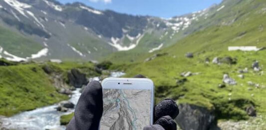 Keine kalten Hände und Füße mehr beim Mountainbiken Hände mit warmen Handschuhen vor einer Bergkullisse die ein Mobiltelefon halten