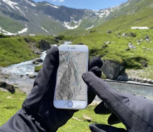 Keine kalten Hände und Füße mehr beim Mountainbiken Hände mit warmen Handschuhen vor einer Bergkullisse die ein Mobiltelefon halten